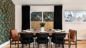 A dining room with a wooden table set for six, surrounded by black chairs, a potted plant, and a view of a wooden fence through large windows. - Arvada Retreat | Garage | Near Olde Town+Red Rocks (Arvada)