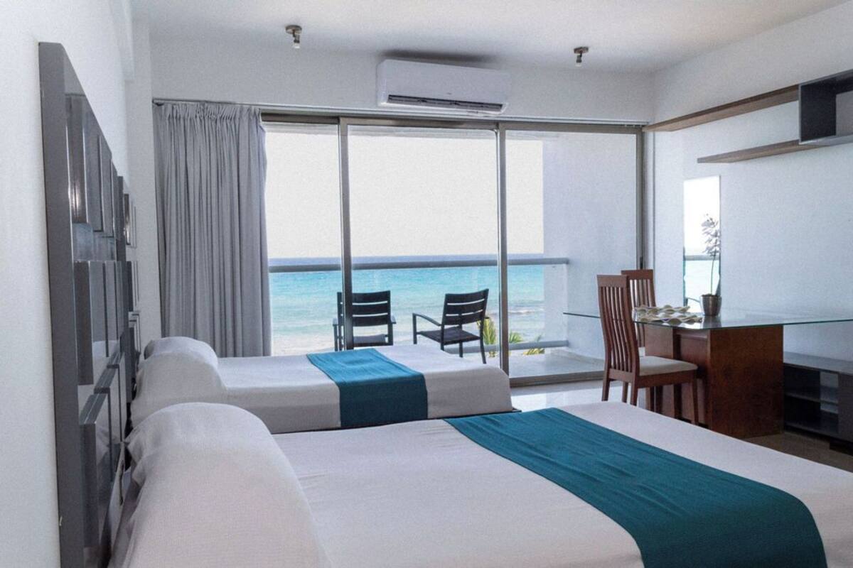 A hotel room with two beds, a desk, and a view of the ocean.