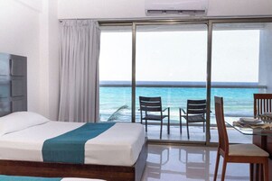 Habitación de hotel con cama, un escritorio y sillas, y vista al océano a través de un amplio ventanal corredero.