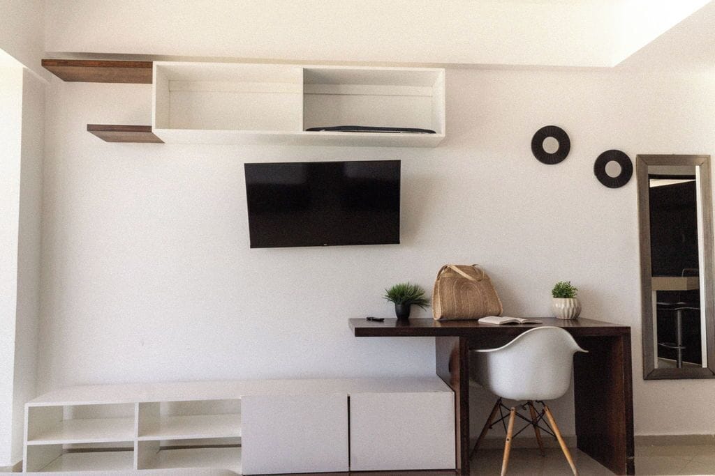 Een moderne kamer met een inbouw bureau, een flatscreen televisie en een zithoek met een stoel en een bankje.