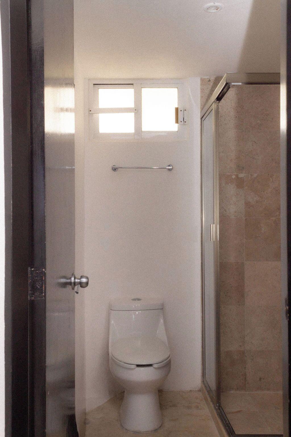 A bathroom with a toilet, a small window, and a shower area.