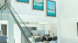 Un intérieur moderne avec un escalier, un espace de vie doté d’un canapé et trois tableaux encadrés représentant des voiliers.