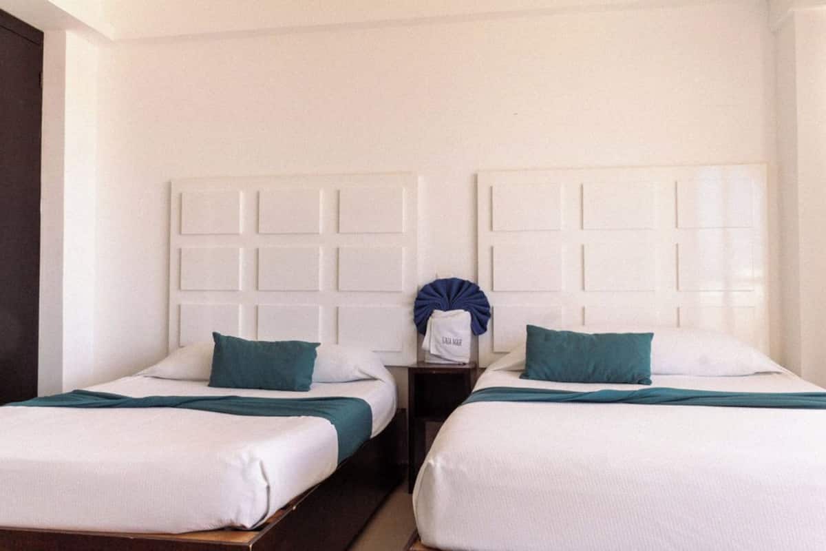 A hotel room with two beds, each with white bedding and teal pillows, and a headboard with a grid pattern.