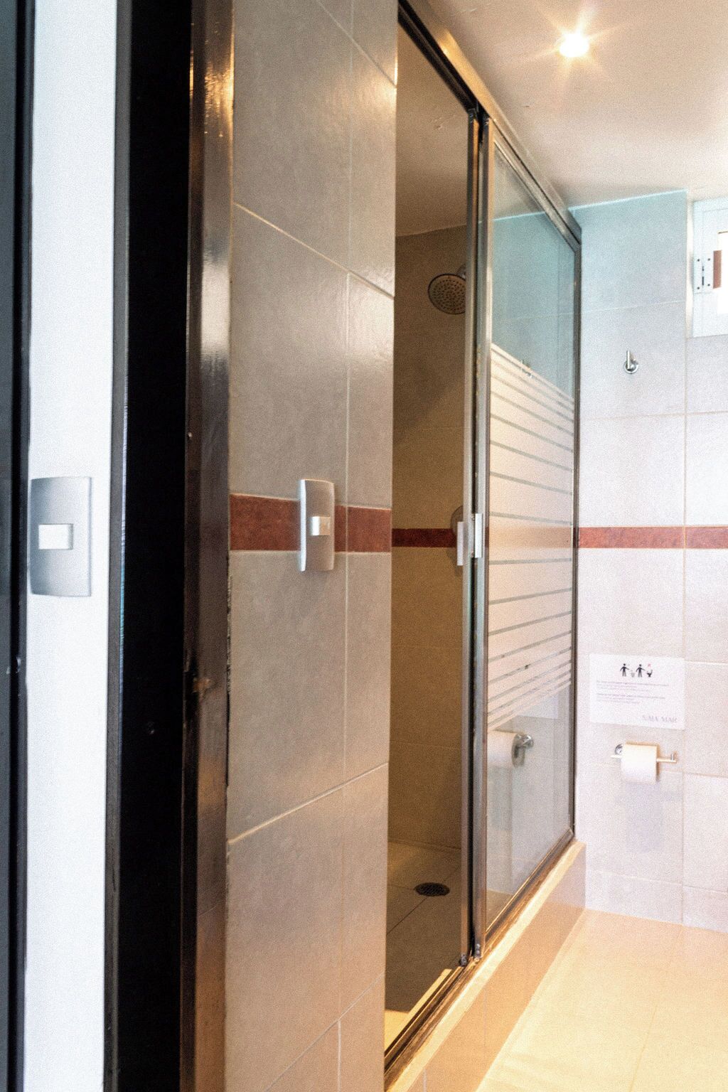 A modern bathroom with a glass shower enclosure, a towel rack, and a hand dryer.