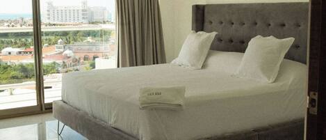 A hotel room with a large bed, a view of the city, and a window with curtains.