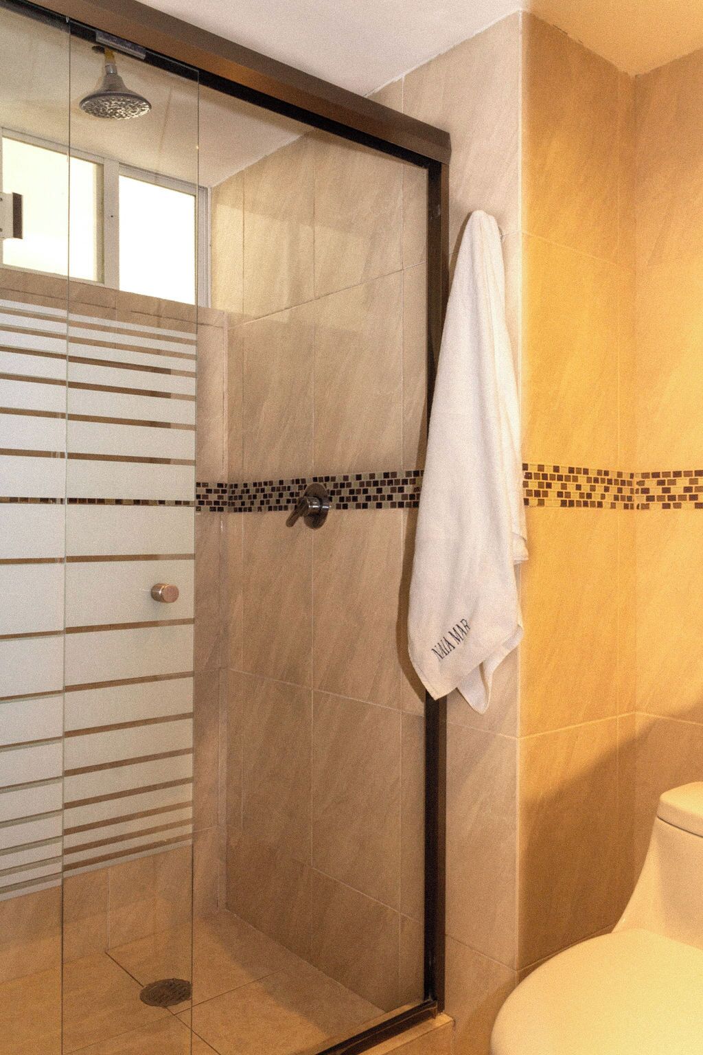 A bathroom with a glass-enclosed shower, a white towel hanging on the wall, and a tiled floor.