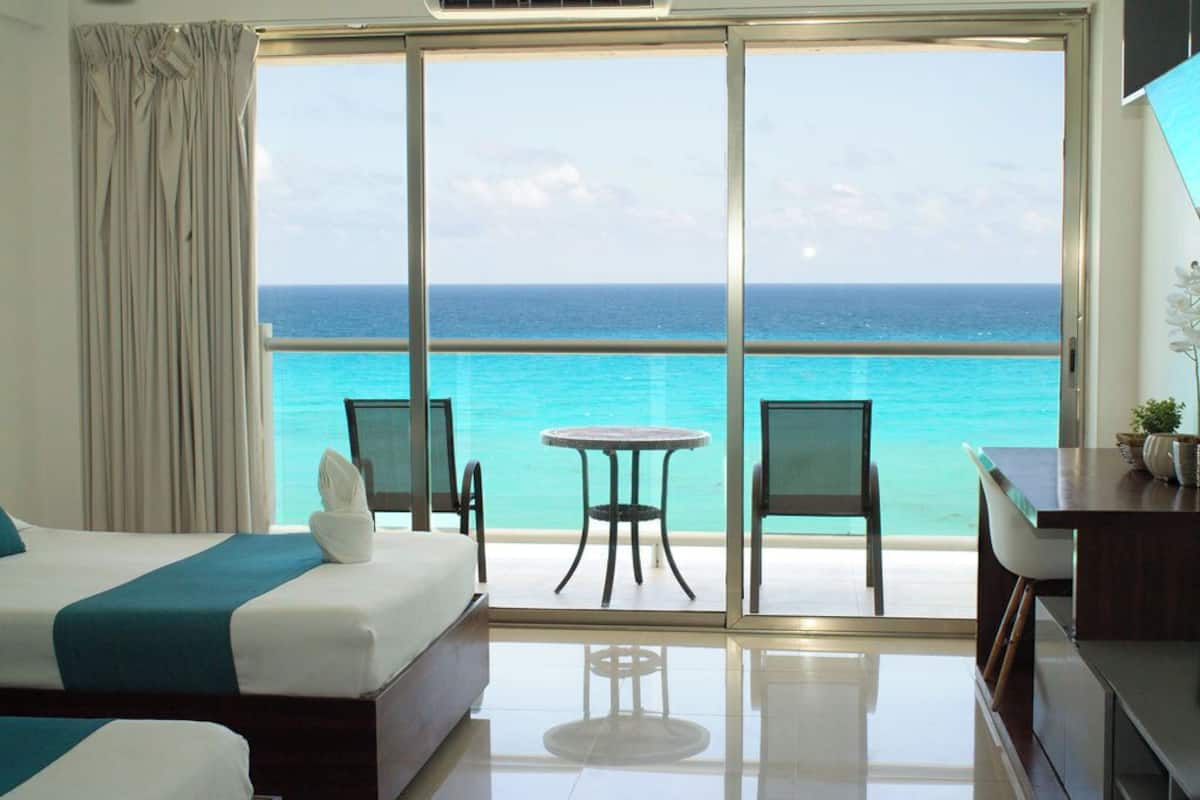 A hotel room with a large balcony, a bed, a table, and chairs.