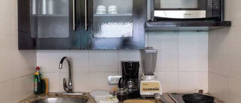 A kitchen with a granite countertop, stainless steel sink, a coffee maker, a blender, a frying pan, and a microwave.