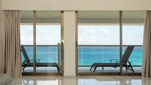 Un salon moderne doté de grandes portes-fenêtres coulissantes qui donnent sur un balcon où se trouvent deux fauteuils confortables, orientés vers l’océan.