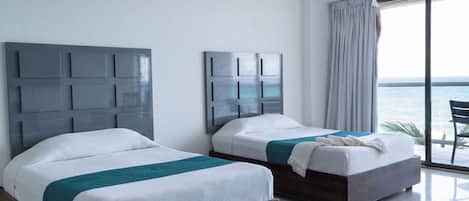 A hotel room with two beds, a large window with a view of the sea, and a balcony with a chair.