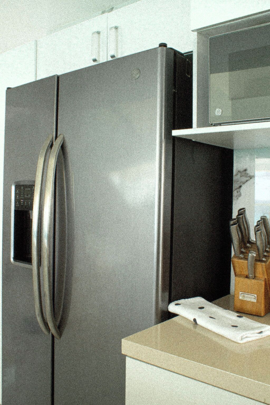 Un refrigerador de acero inoxidable con un microondas integrado encima, y un bloque para cuchillos en la encimera.
