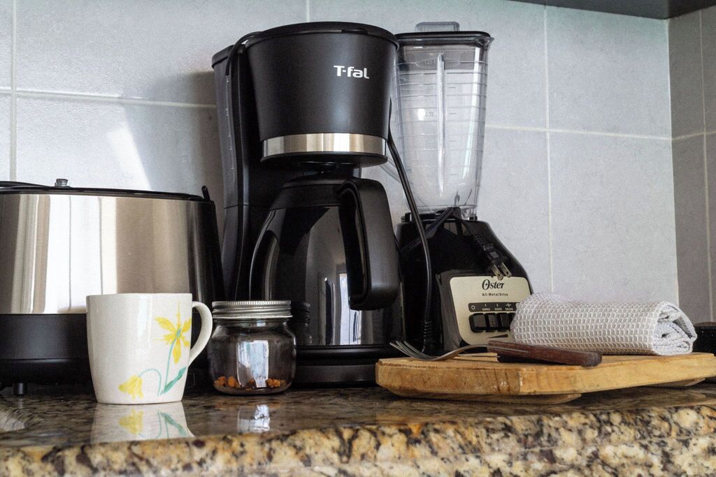 Une cuisine équipée d’une machine à café, d’un mixeur et d’une tasse posée sur le comptoir.
