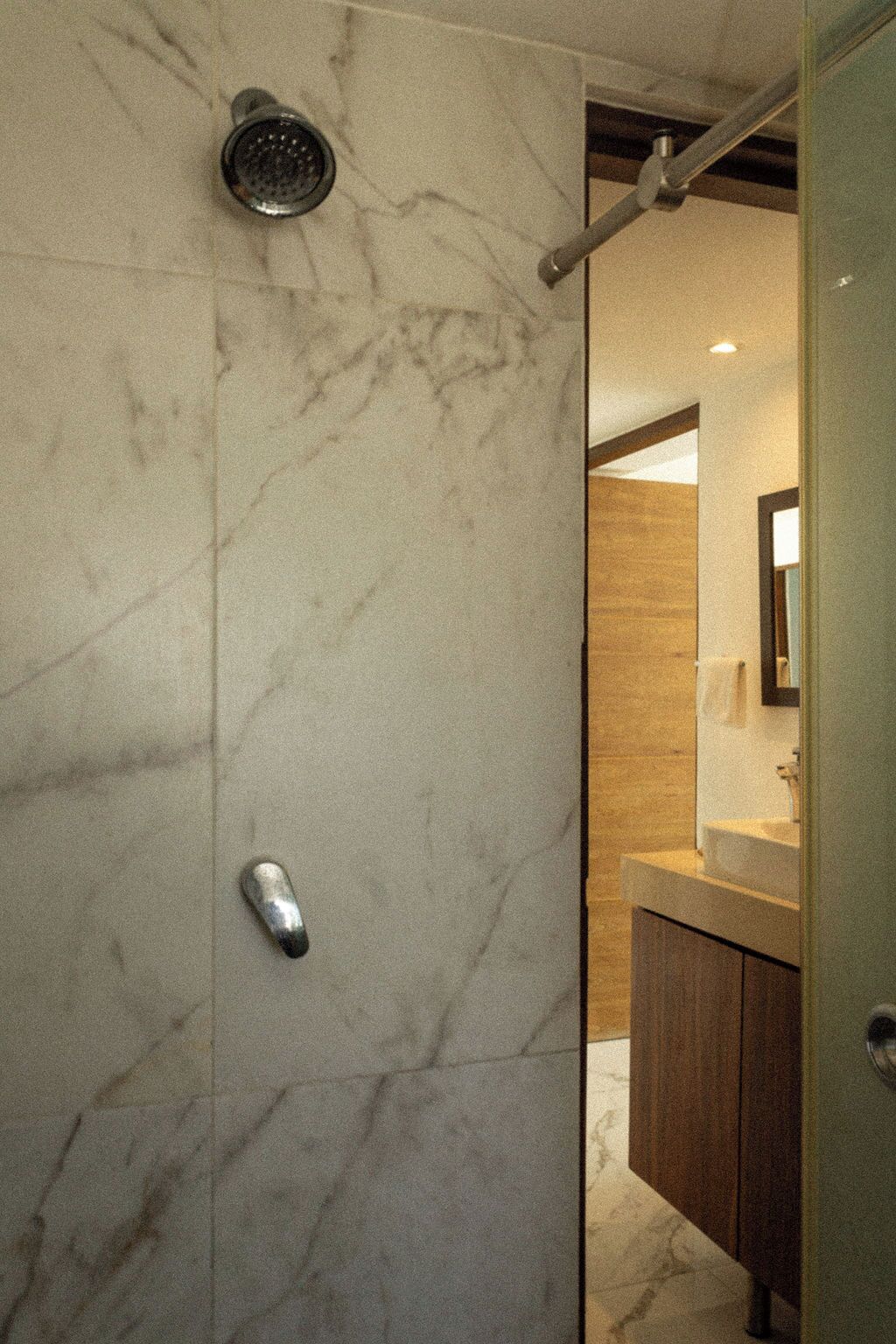 A bathroom with a marble wall, a showerhead, and a wooden door.