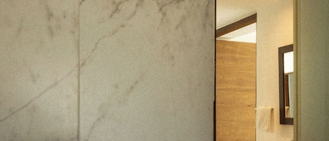Un baño con pared de mármol, un cabezal de ducha y una puerta de madera.