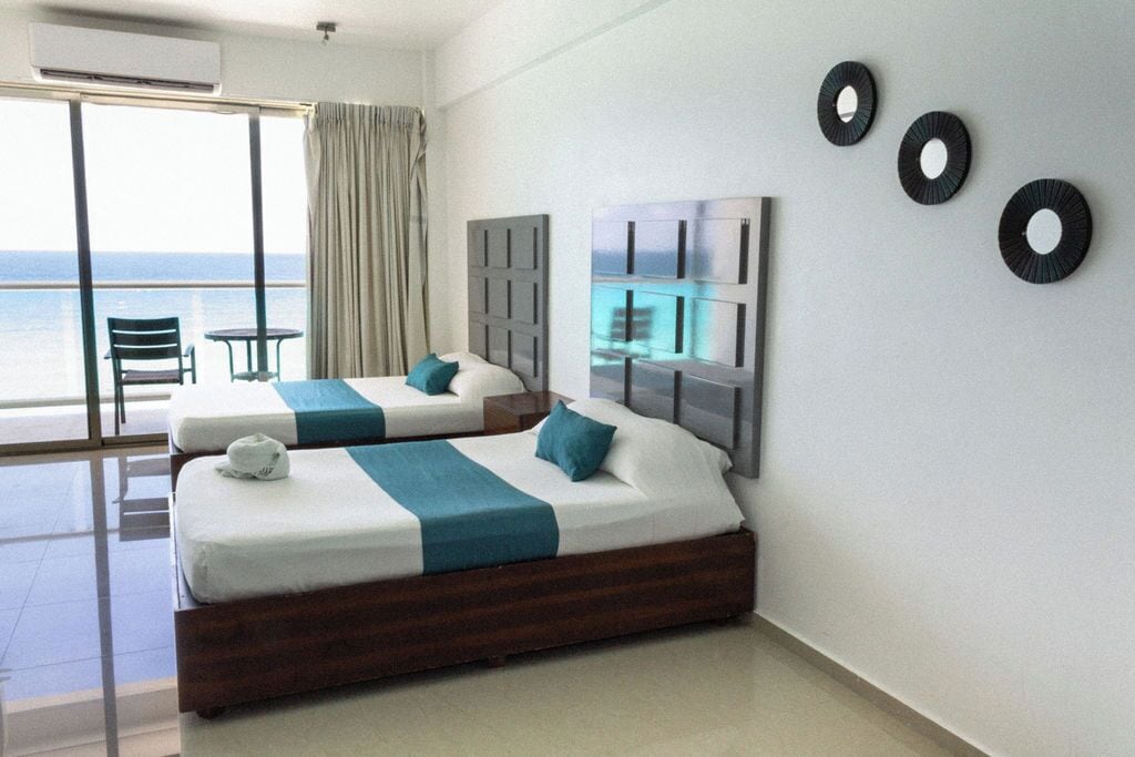 A hotel room with two beds, a balcony with a view of the sea, and a large window.