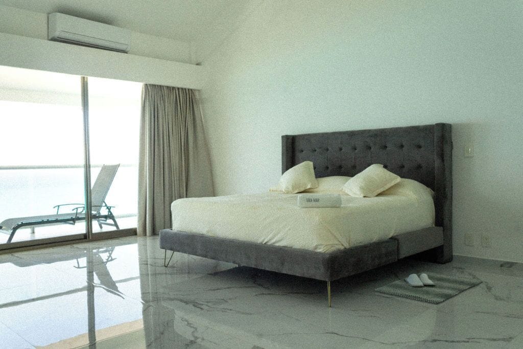 A modern bedroom with a large bed, a glass floor, and a view of the sea.