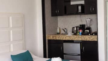 Habitación de hotel con dos camas, kitchenette y cabecera blanca.