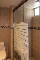 Un bagno con box doccia in vetro, un water e pareti rivestite di piastrelle.