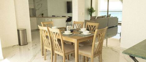 Un comedor moderno con una mesa y sillas de madera, una cocina al fondo y vista al mar.