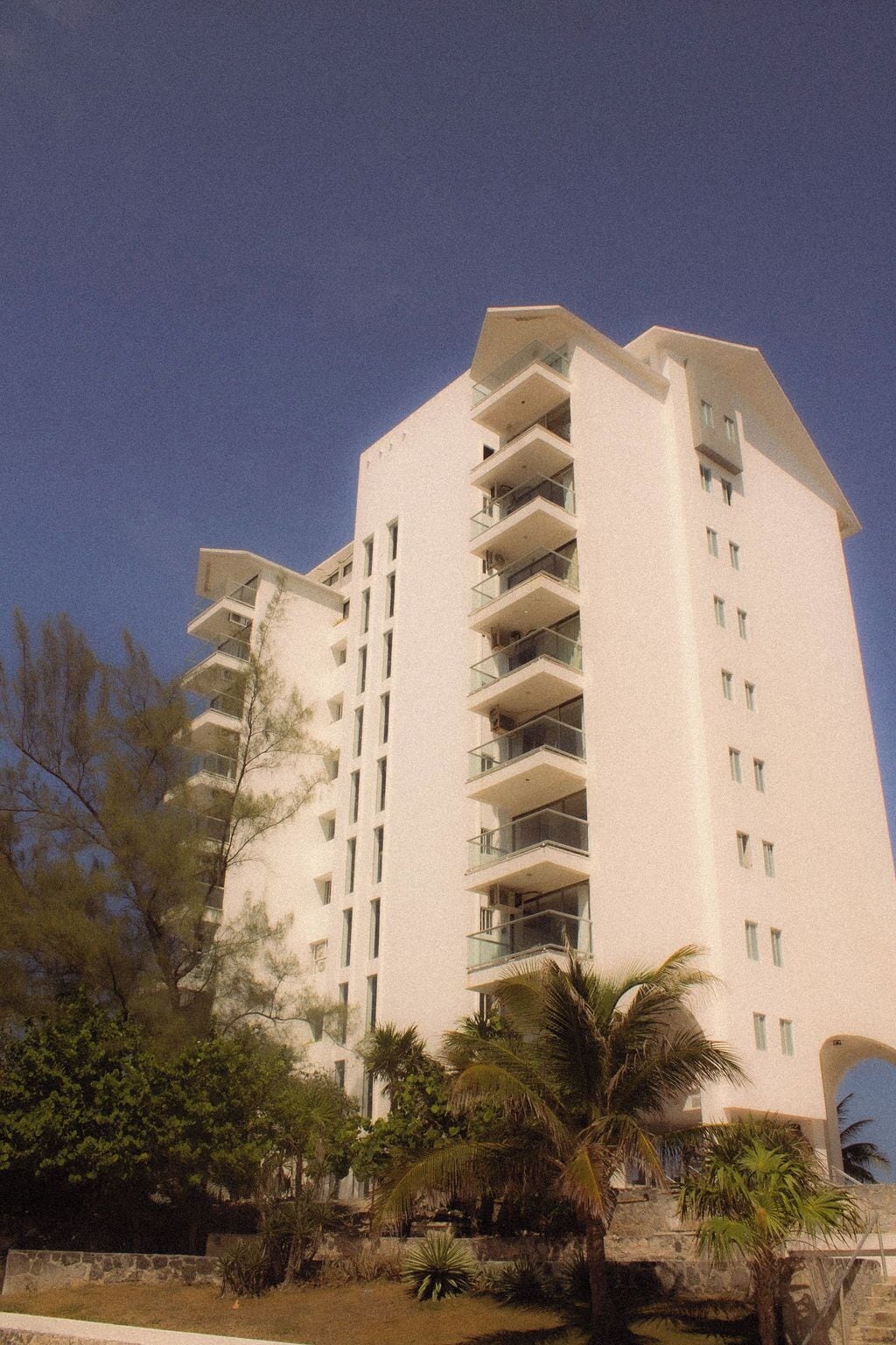 Un hotel de varios pisos con balcones y un jardín con palmeras.