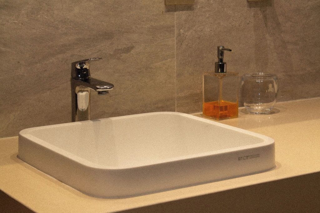 A bathroom with a white sink, a soap dispenser, and a glass.