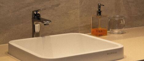 A bathroom with a white sink, a soap dispenser, and a glass.