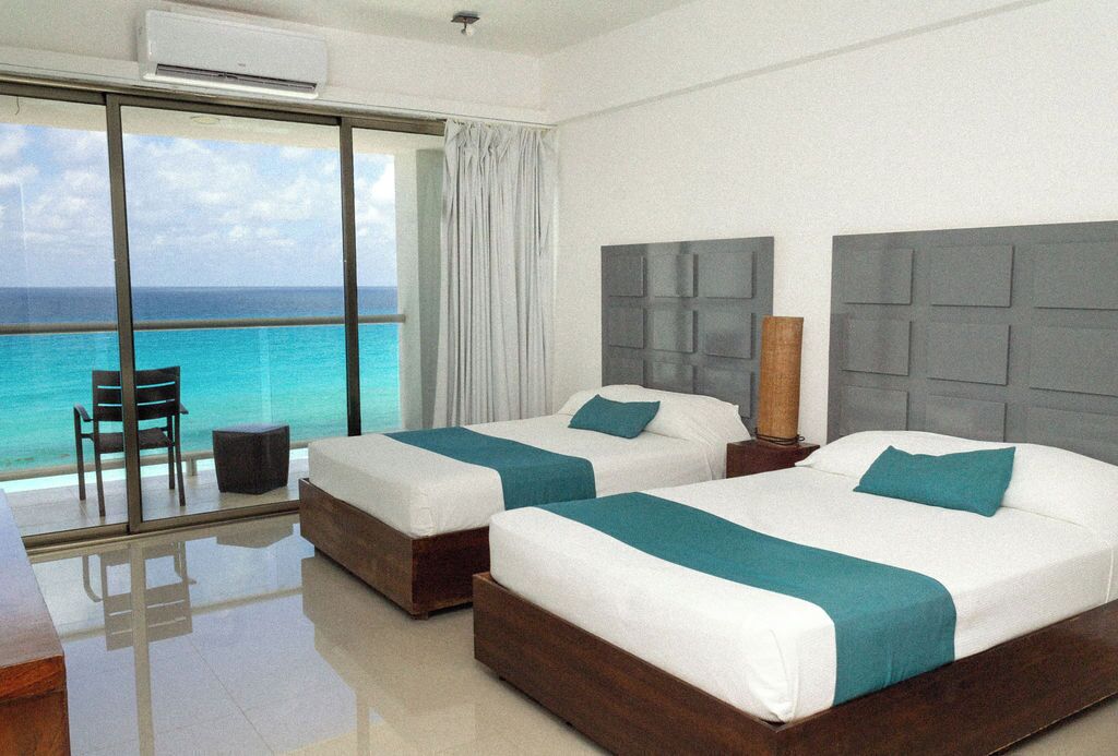 A hotel room with two beds, a large window with a view of the ocean, a chair, and a table.