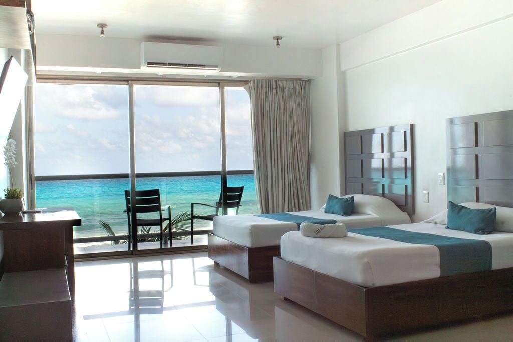 A hotel room with two beds, a desk, and a view of the ocean.