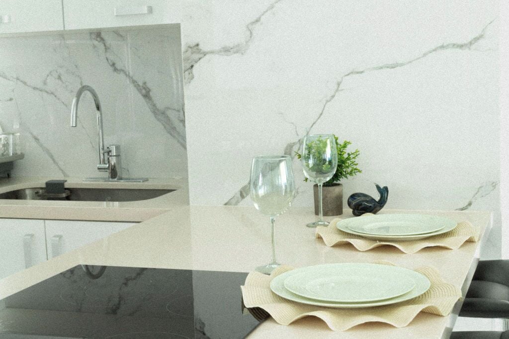 Une cuisine moderne avec un dosseret en marbre, un évier encastré et une table à manger en verre, agrémentée d’un chemin de table décoratif.