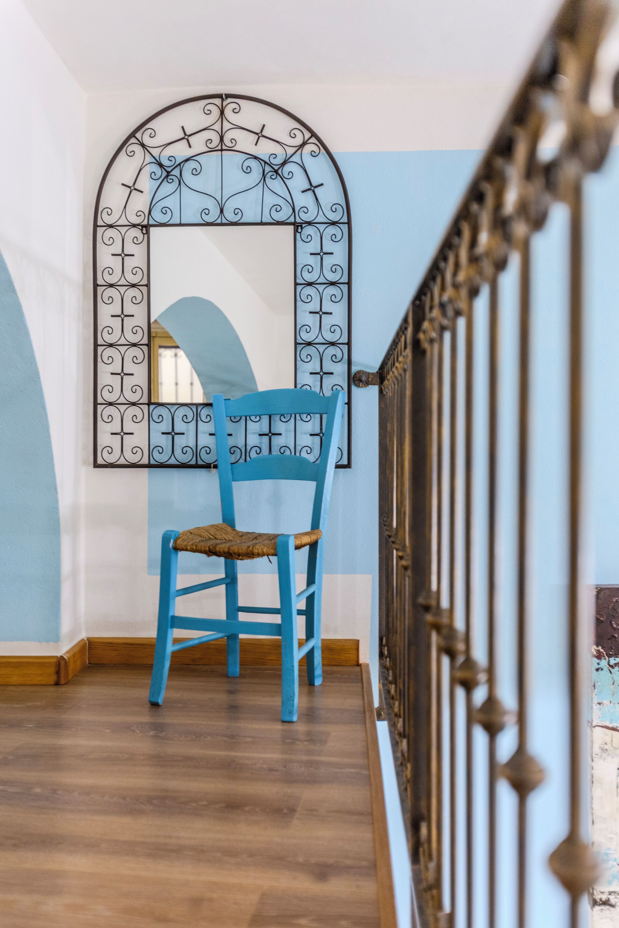Une chaise bleue se trouve dans un couloir, agrémenté d’une arche décorative en métal et doté d’un plancher en bois.