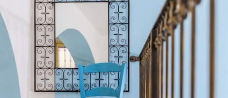 A blue chair in a hallway with a decorative metal archway and a wooden floor.