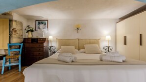 Ein Schlafzimmer mit Bett, Nachttischlampen, Kommode, Stuhl und Wandventilator.