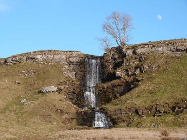 Una cascada se precipita por un acantilado rocoso rodeado de terreno cubierto de pasto.