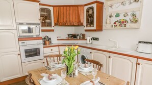 Een keuken met witte kasten, houten aanrecht, een eettafel gedekt voor vier personen en een wasmachine.