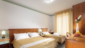 Hotellihuone, jossa on kaksi sänkyä, puinen pääty, työpöytä, jossa on maljakko täynnä kukkia, ja hedelmäkulho.