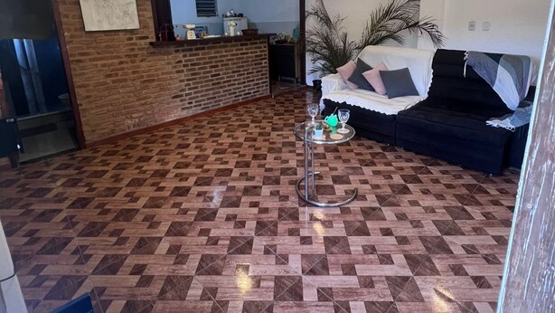 Ein geräumiger Wohnbereich mit einem gemusterten Holzboden, einem schwarzen Sofa und einem kleinen runden Tisch mit zwei Gläsern.