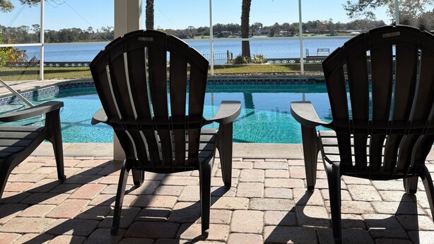 Un espace extérieur abrité, doté de deux fauteuils Adirondack donnant sur une piscine et offrant une vue sur un lac.