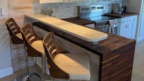 Une cuisine moderne avec des meubles blancs, un îlot central en bois doté de tabourets, des luminaires suspendus et des appareils électroménagers en acier inoxydable.