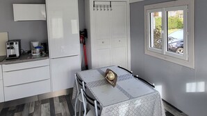 A compact room with a kitchenette, a dining table with chairs, a wardrobe, and a window with a view of a car and greenery outside. - Nature getaway: cottage with grounds (Saint antheme)