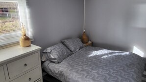 A bedroom with a bed, a dresser, a nightstand, a lamp, and a window with blinds. - Nature getaway: cottage with grounds (Saint antheme)
