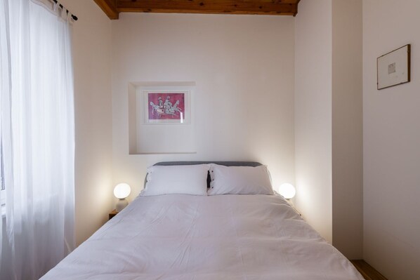 A bedroom with a bed, two bedside lamps, a window with curtains, and a framed picture on the wall. - Trastevere Luxury Panoramic Apartment (Roma)