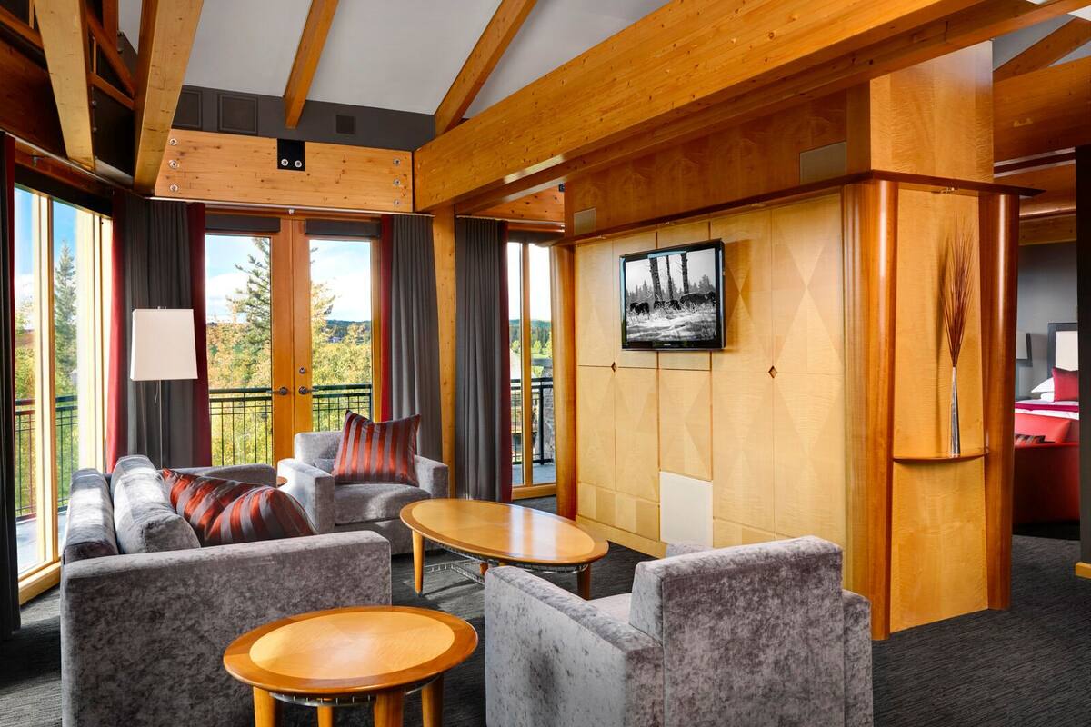 A modern interior with a wooden ceiling, grey upholstered seating, and a large window offering a scenic view.