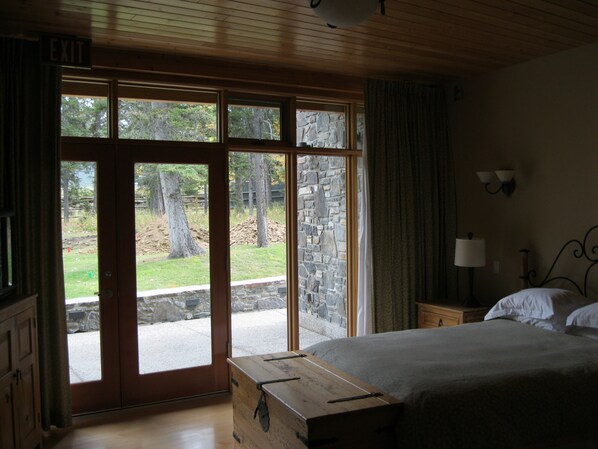 A bedroom with a large window, a bed, a dresser, and a nightstand. - Azuridge Estate Hotel (Priddis)