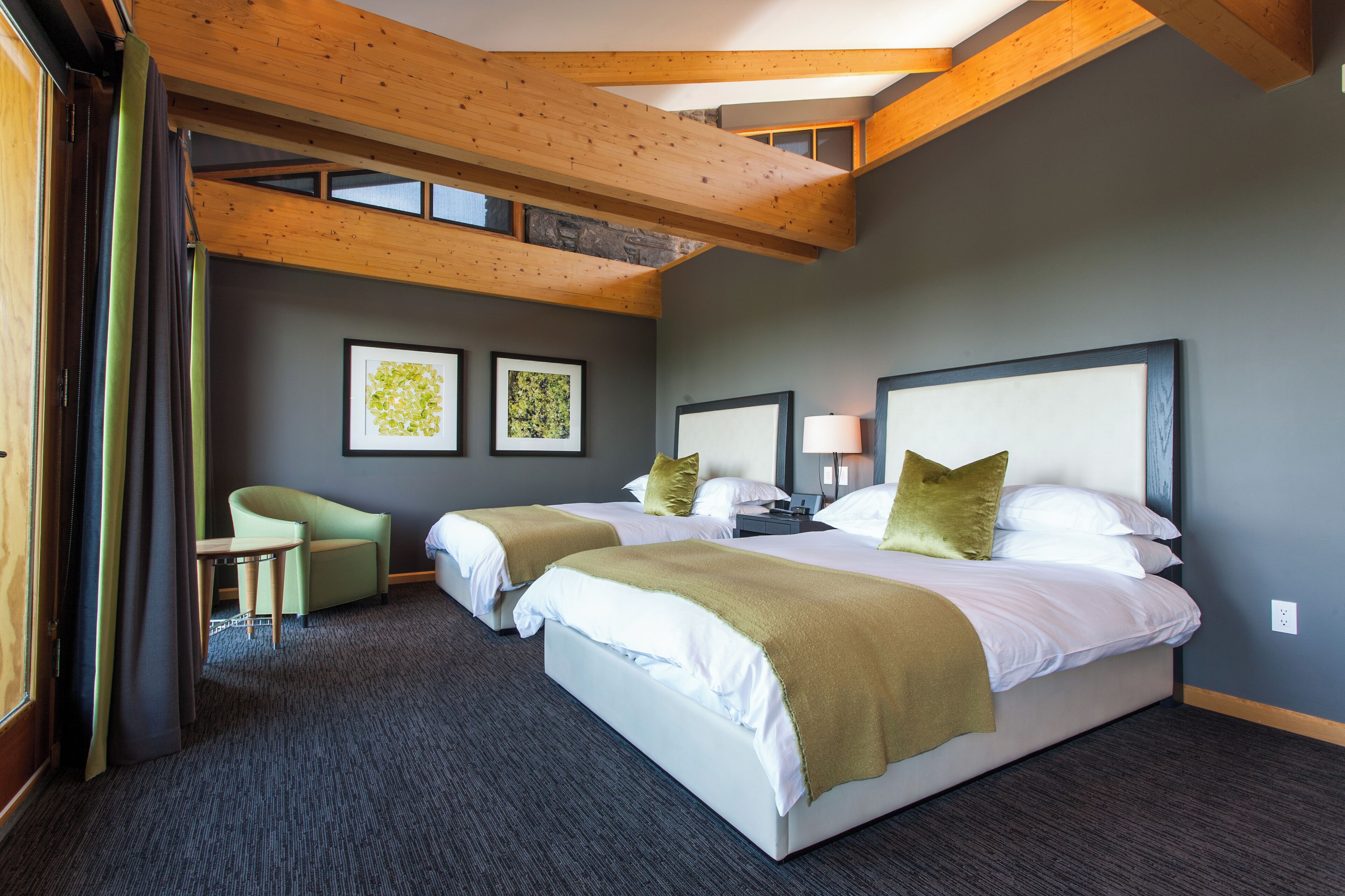 Una habitación de hotel moderna con dos camas, un sillón verde y una mesita.