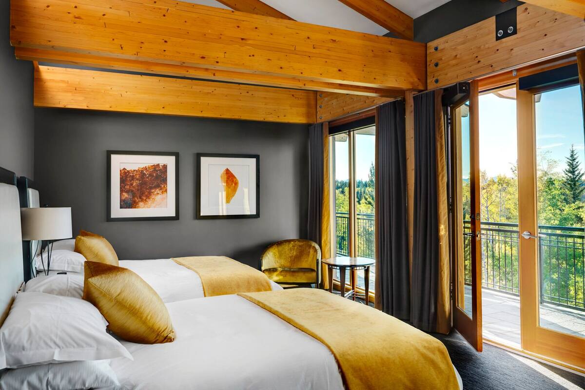 A hotel room with a large bed, two chairs, a small table, and a balcony with a view of trees.