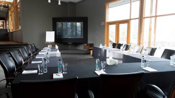 Un salón de conferencias con una larga mesa, sillas, una pantalla de televisión y ventanas amplias.
