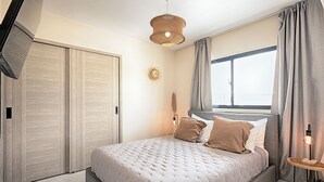 Et soveværelse med seng, et natbord med lampe, et vindue med gardiner og et klædeskab.