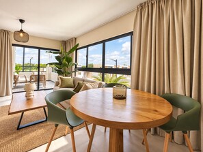 A modern living room with a round wooden table, green chairs, a sofa, and a large window with curtains. - A Peaceful Retirement in Punta Cana (Punta Cana)