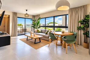 A modern living room with a sofa, coffee table, and chairs, a dining table with chairs, large windows with a view, and a flat-screen TV. - A Peaceful Retirement in Punta Cana (Punta Cana)