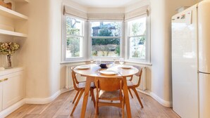Eine Küche mit Erkerfenster, einem Holzespeisetisch, Stühlen und einem Kühlschrank.
